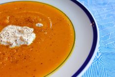 a white plate topped with soup and cream on top of a blue table cloth next to a spoon