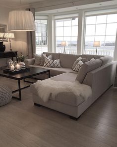 a living room filled with lots of furniture next to large windows on top of a hard wood floor