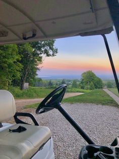 a golf cart driving down a gravel road at sunset with the sun setting in the distance