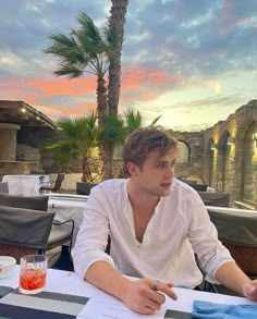 a man sitting at a table with a drink in front of him and looking off into the distance