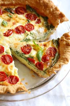 a quiche with tomatoes and spinach is on a glass plate, ready to be eaten