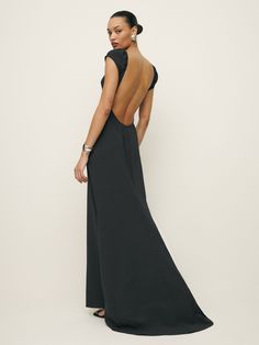 the back of a woman wearing a long black dress with an open back and cutout