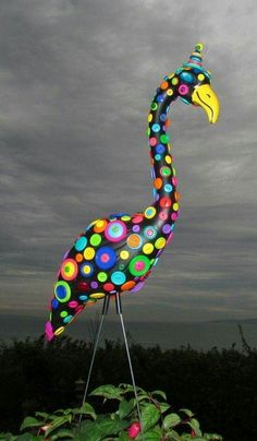 a tall colorful bird statue sitting on top of a lush green field under a cloudy sky