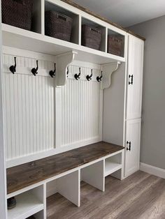 a white mud room with some benches and baskets on the wall, along with other storage units