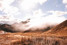 the sun shines brightly on an open field with tall grass and mountains in the background