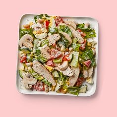 a white plate topped with salad and meat on top of a pink background, next to a fork