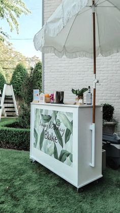 an outdoor ice cream stand with white umbrella and greenery on the outside, in front of a brick building