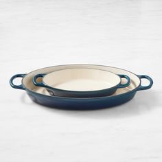 two blue oval casserole dishes sitting on a white countertop with marble background