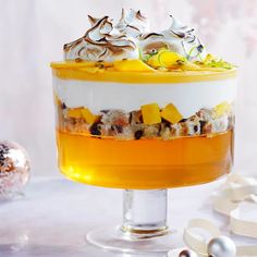 an orange and white layered dessert on a cake stand with silver ornaments around it,