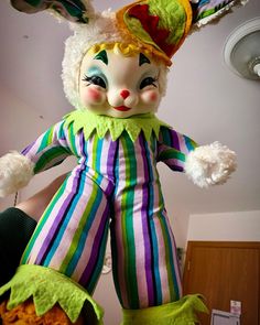 a close up of a stuffed animal wearing a clown suit and hat on top of a bed