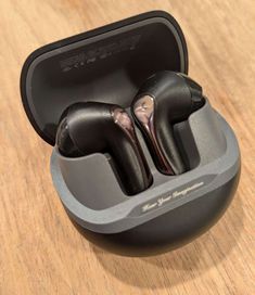 two black earbuds sitting in an open case on a wooden table with the lid closed