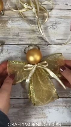 someone is holding some gold balls in their hand and wrapping them around the christmas ornament