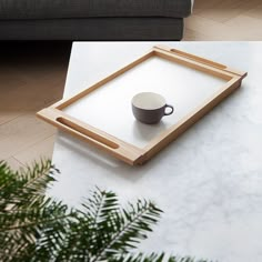 a coffee cup sitting on top of a white table next to a wooden framed tray