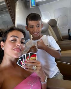 a woman holding up cards next to a young boy on an airplane with the seat belt down