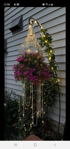 a birdcage with lights hanging from it's sides and flowers in the bottom