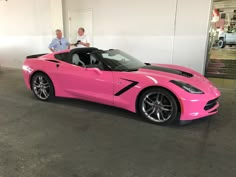 two men standing next to a pink sports car