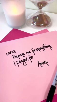 a pink note sitting on top of a table next to a candle