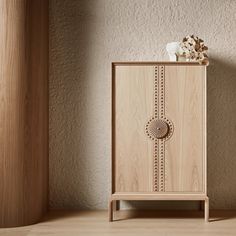 a wooden cabinet sitting next to a vase with flowers in it on top of a hard wood floor