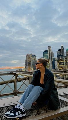 a woman sitting on top of a wooden bench next to the ocean and tall buildings