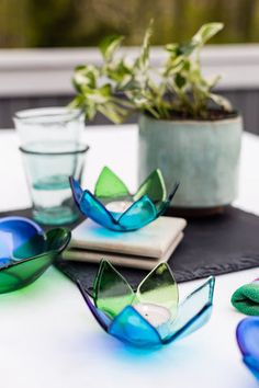 some blue and green glasses sitting on top of a white table next to a potted plant