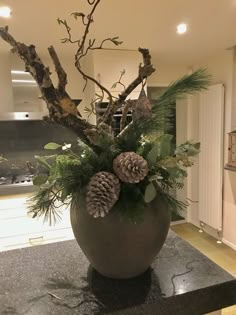 a vase filled with pine cones and greenery sitting on top of a black counter