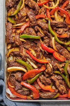 a pan filled with meat and peppers on top of a table next to a blue towel