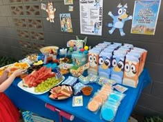 a child standing in front of a blue table with food on it that includes grapes, watermelon and other snacks