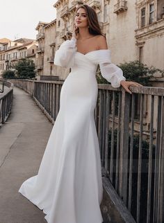 a woman in a white dress is standing on a bridge and talking on her cell phone