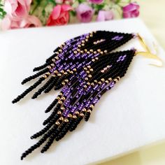 purple and black seed beaded earrings sitting on top of a piece of white paper