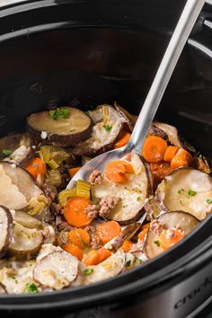 a slow cooker filled with potatoes, carrots and other vegetables being stirred by a spoon