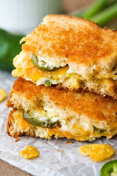 two grilled cheese sandwiches stacked on top of each other with green peppers and jalapenos in the background