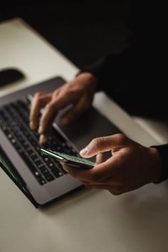 a person holding a cell phone and typing on a laptop