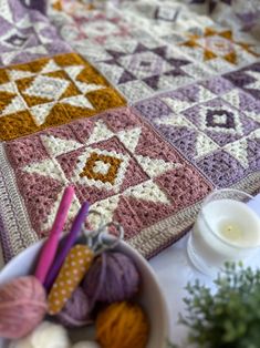 a crocheted table runner with yarn and knitting needles on it next to a bowl of balls of yarn