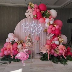 a pink and gold wedding cake surrounded by flamingos, palm leaves, and balloons