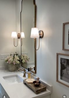 a bathroom sink with two lights on the wall above it and pictures hanging on the wall