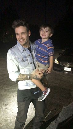 a man holding a little boy in his arms while standing on the street at night