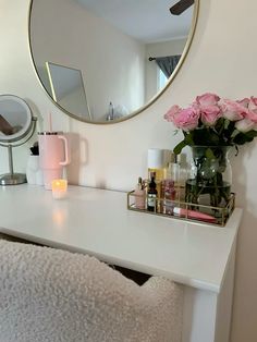 a white vanity with pink roses and candles on it in front of a round mirror