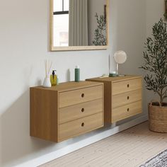 a wooden dresser sitting next to a mirror on top of a white wall near a potted plant