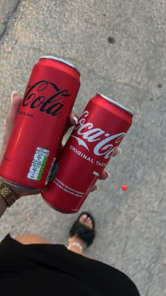 a woman holding two coca cola cans in her hand