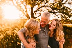 an older man and two young women hugging each other in a field with trees behind them