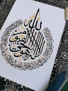 an arabic calligraphy is displayed on a white paper with black and gold lettering,