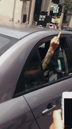 a hand sticking out of the window of a car while holding up a cell phone