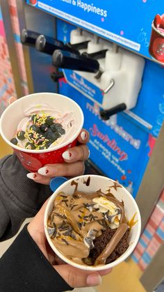 two people holding up bowls of food in front of a vending machine