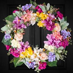 a wreath with flowers and greenery hanging on a door