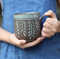 a person holding a coffee cup in their hands with leaves on it's side