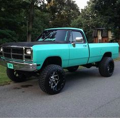 a bright blue truck parked on the side of a road next to some grass and trees