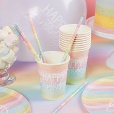 a table topped with plates and cups filled with cake next to a rainbow colored balloon