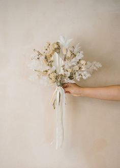 a person holding a bunch of flowers in their hand on a beige background with white ribbon