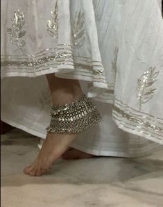 a woman's feet with silver beaded barefoot sandals on top of her legs