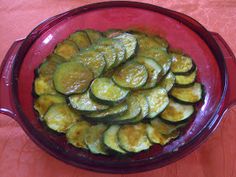 a red bowl filled with sliced cucumbers on top of a wooden tablecloth